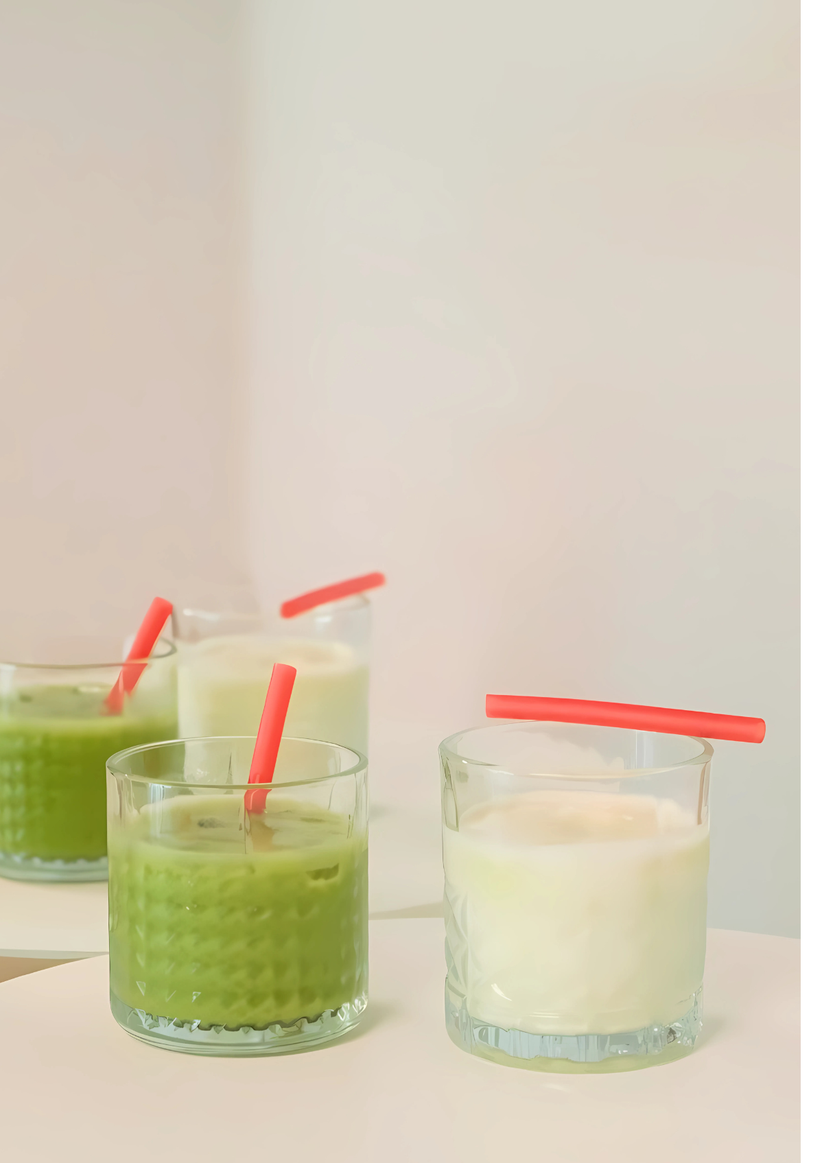 Two glasses with beverages, one green and one white, each with a red rice straw on top.