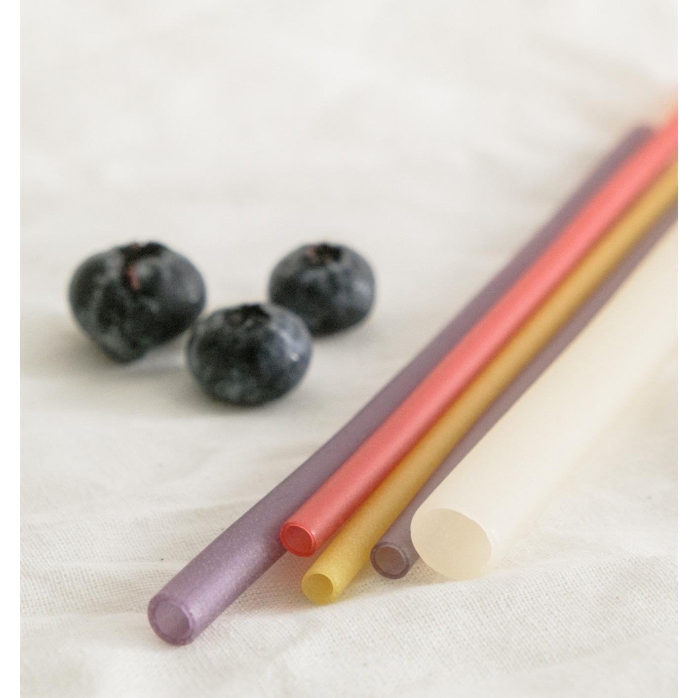 Colorful biodegradable rice straws with blueberries on a white surface, eco-friendly alternative to plastic straws.
