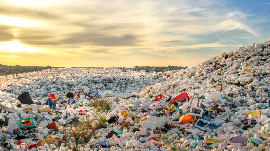 A large pile of plastic waste and debris against a sunset sky, illustrating the environmental impact of plastic pollution.